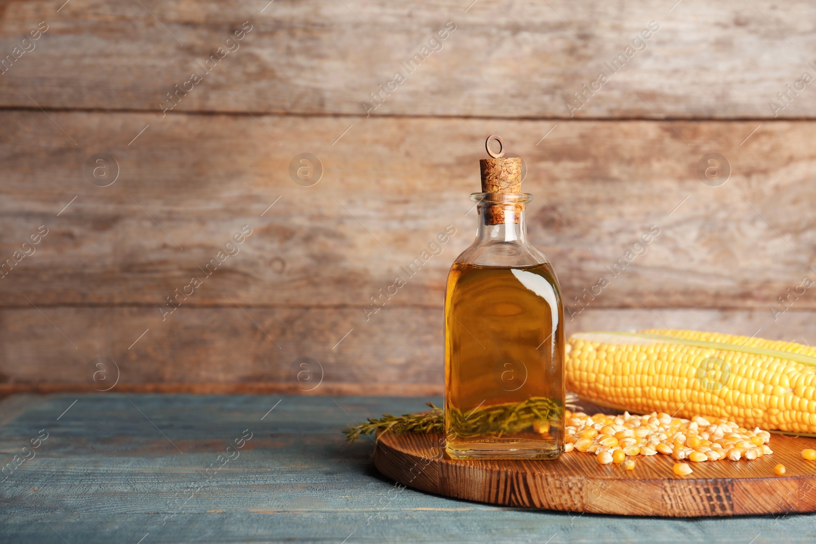 Photo of Bottle of corn oil and fresh cobs on table against wooden wall