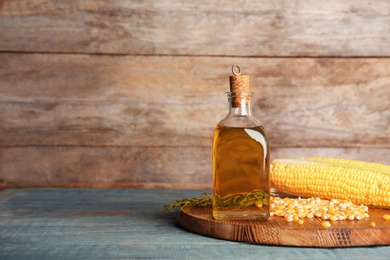 Bottle of corn oil and fresh cobs on table against wooden wall