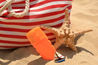 Photo of Bottle of sunscreen, starfish, and bag on sand, closeup. Sun protection care