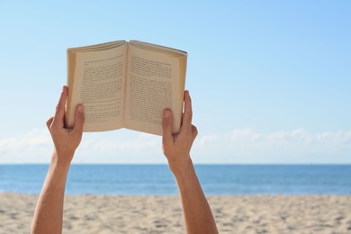 Woman reading book on beach near sea, closeup. Space for text