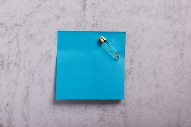Photo of Blue paper note with safety pin on grey textured background, top view