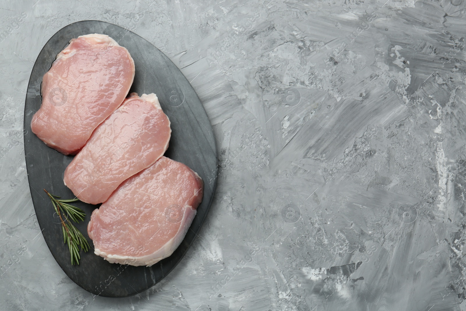 Photo of Pieces of raw pork meat and rosemary on grey textured table, top view. Space for text