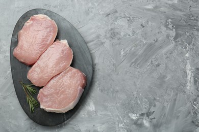 Photo of Pieces of raw pork meat and rosemary on grey textured table, top view. Space for text