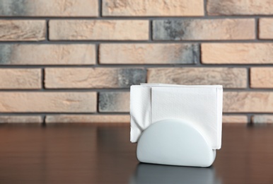 Photo of Ceramic napkin holder with paper serviettes on table near brick wall. Space for text