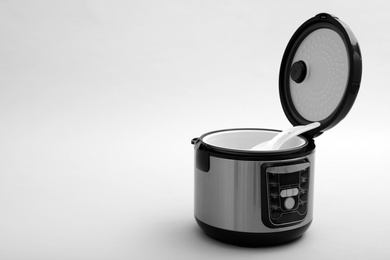 Photo of Modern electric multi cooker with spoon and ladle on grey background. Space for text