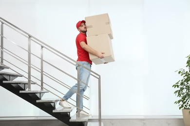 Photo of Man in uniform carrying carton boxes downstairs indoors. Posture concept