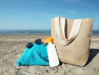 Photo of Bag with sunglasses, towel and sun protection product on sandy beach