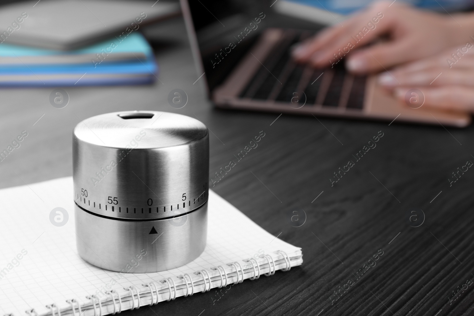 Photo of Woman working on laptop at wooden table, focus on kitchen timer. Space for text