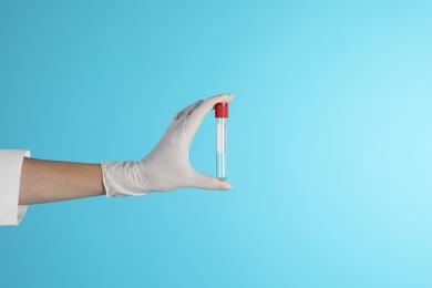 Photo of Female doctor holding empty test tube on color background, closeup view with space for text. Medical object