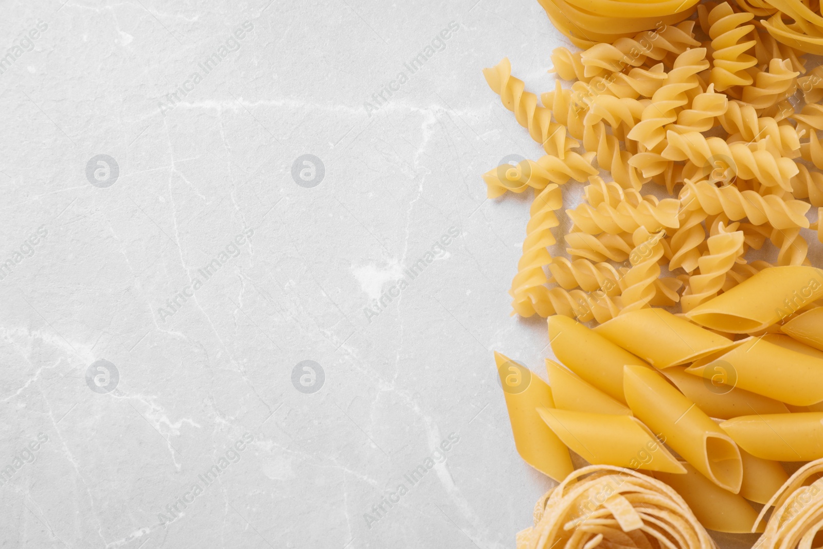 Photo of Different types of pasta on light grey marble table, flat lay. Space for text