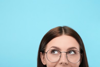 Woman in stylish eyeglasses on light blue background, closeup. Space for text