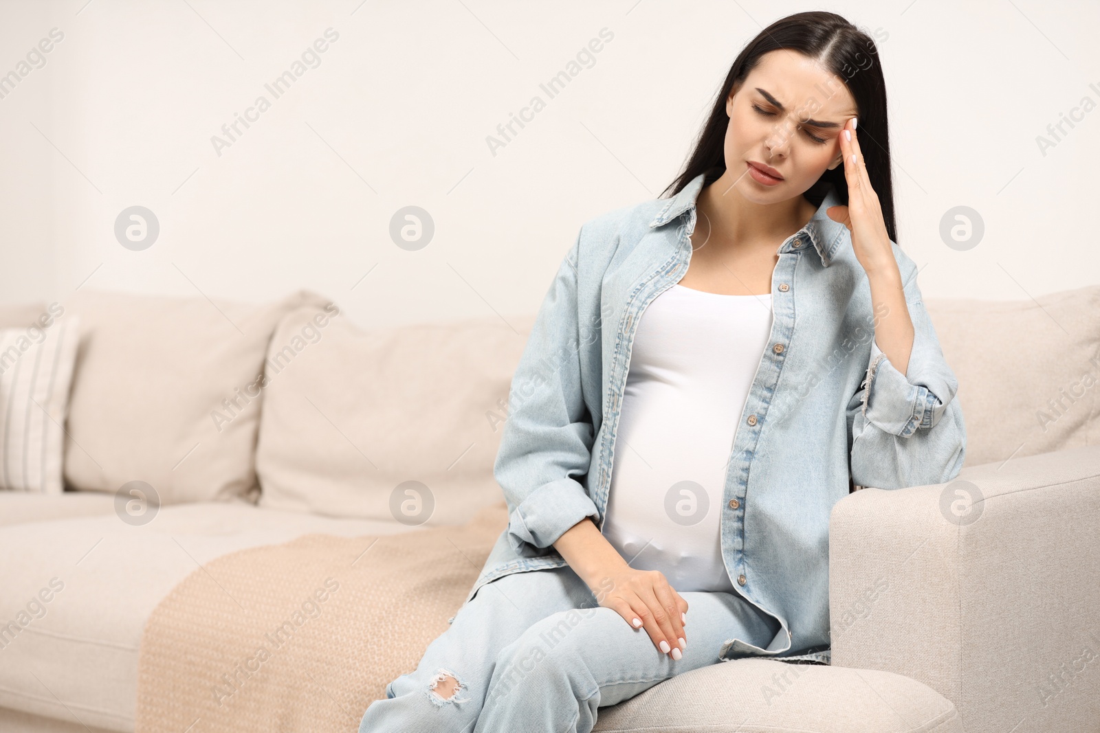 Photo of Pregnant woman suffering from headache on sofa at home, space for text