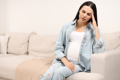 Pregnant woman suffering from headache on sofa at home, space for text