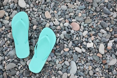 Stylish turquoise flip flops on pebble seashore, top view. Space for text