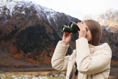 Woman looking through binoculars in beautiful mountains. Space for text