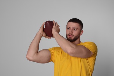 Athletic young man with American football ball on light grey background