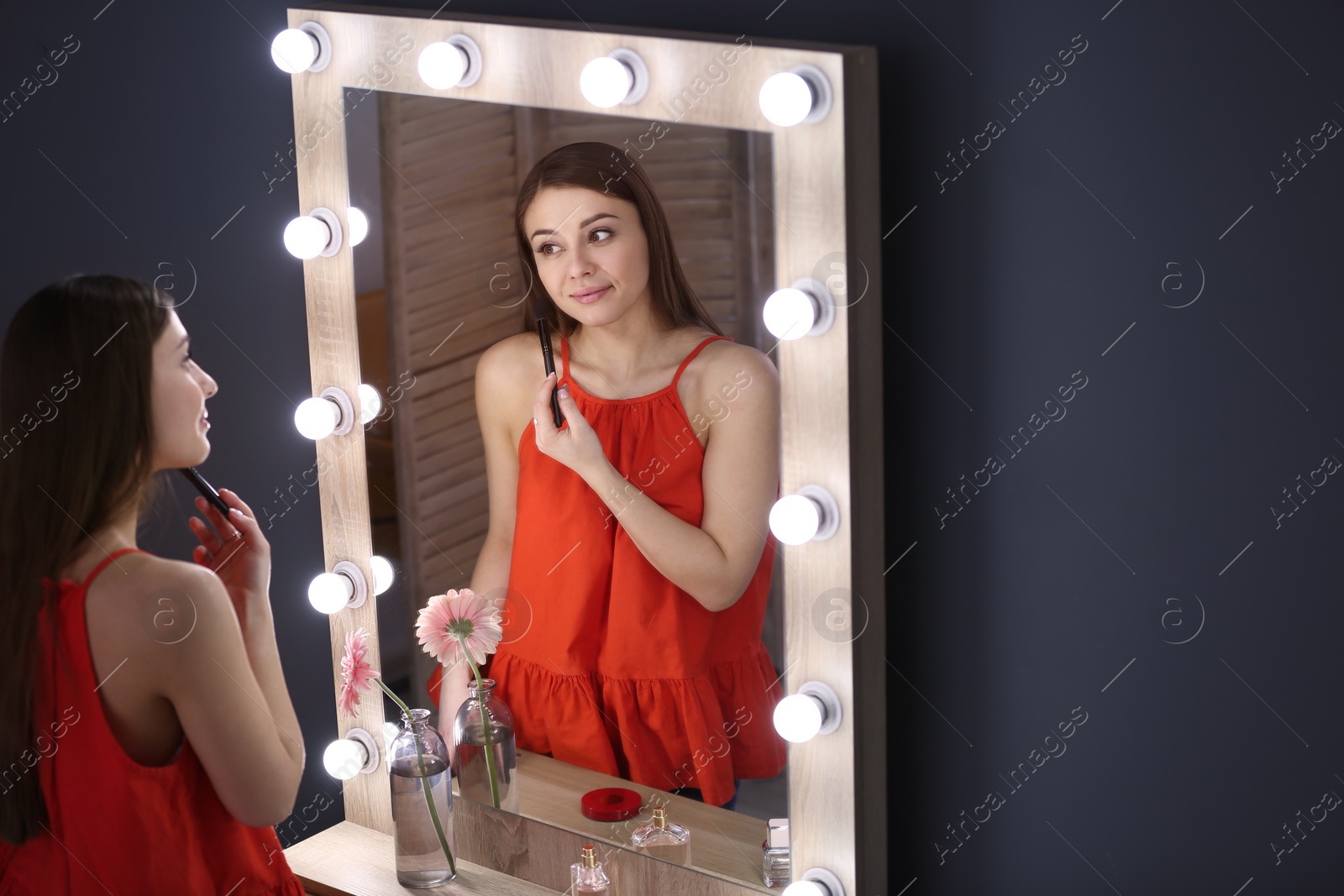 Photo of Young beautiful woman applying makeup near mirror