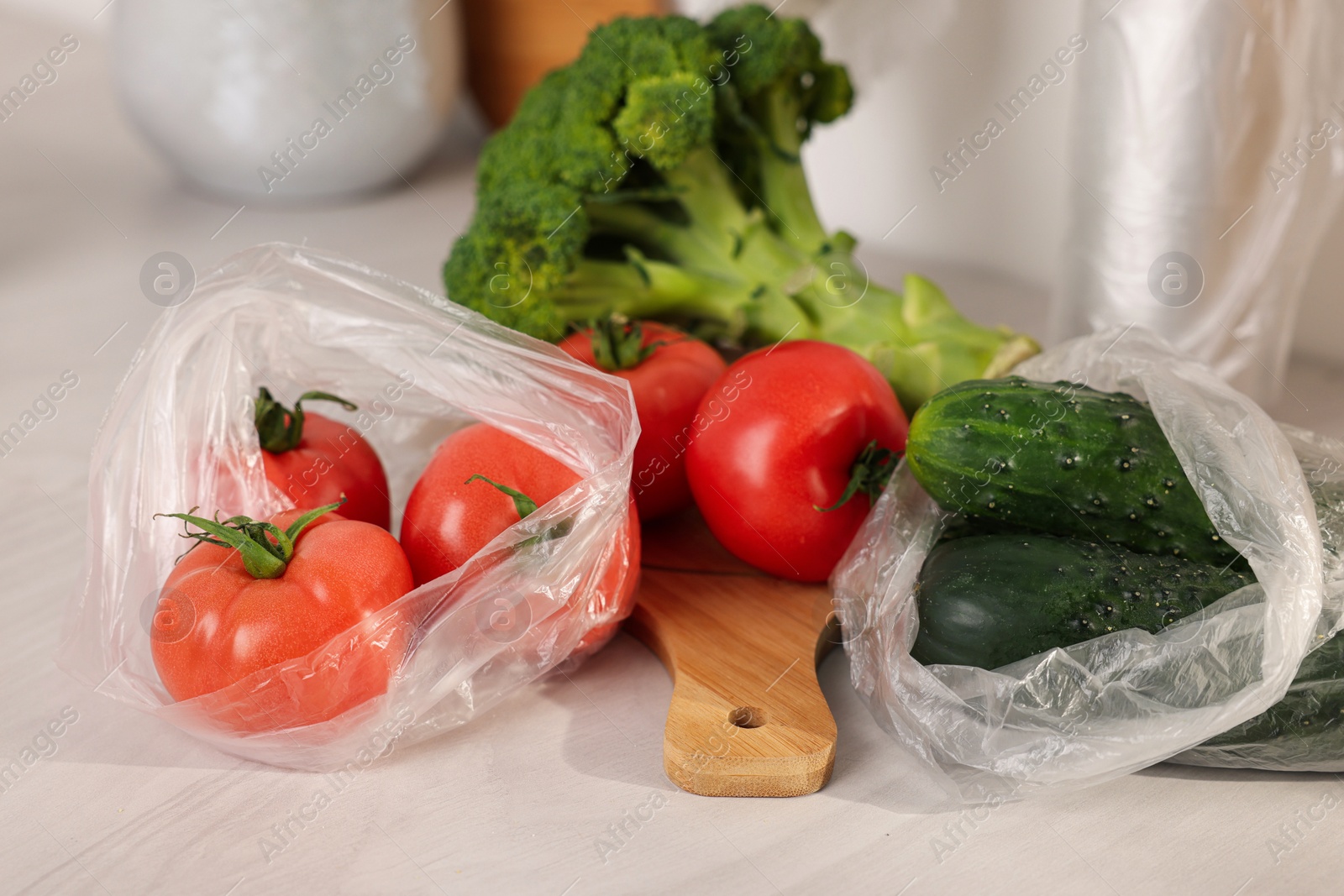 Photo of Plastic bags and fresh vegetables on white table, closeup