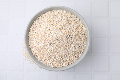 Dry barley groats in bowl on white tiled table, top view