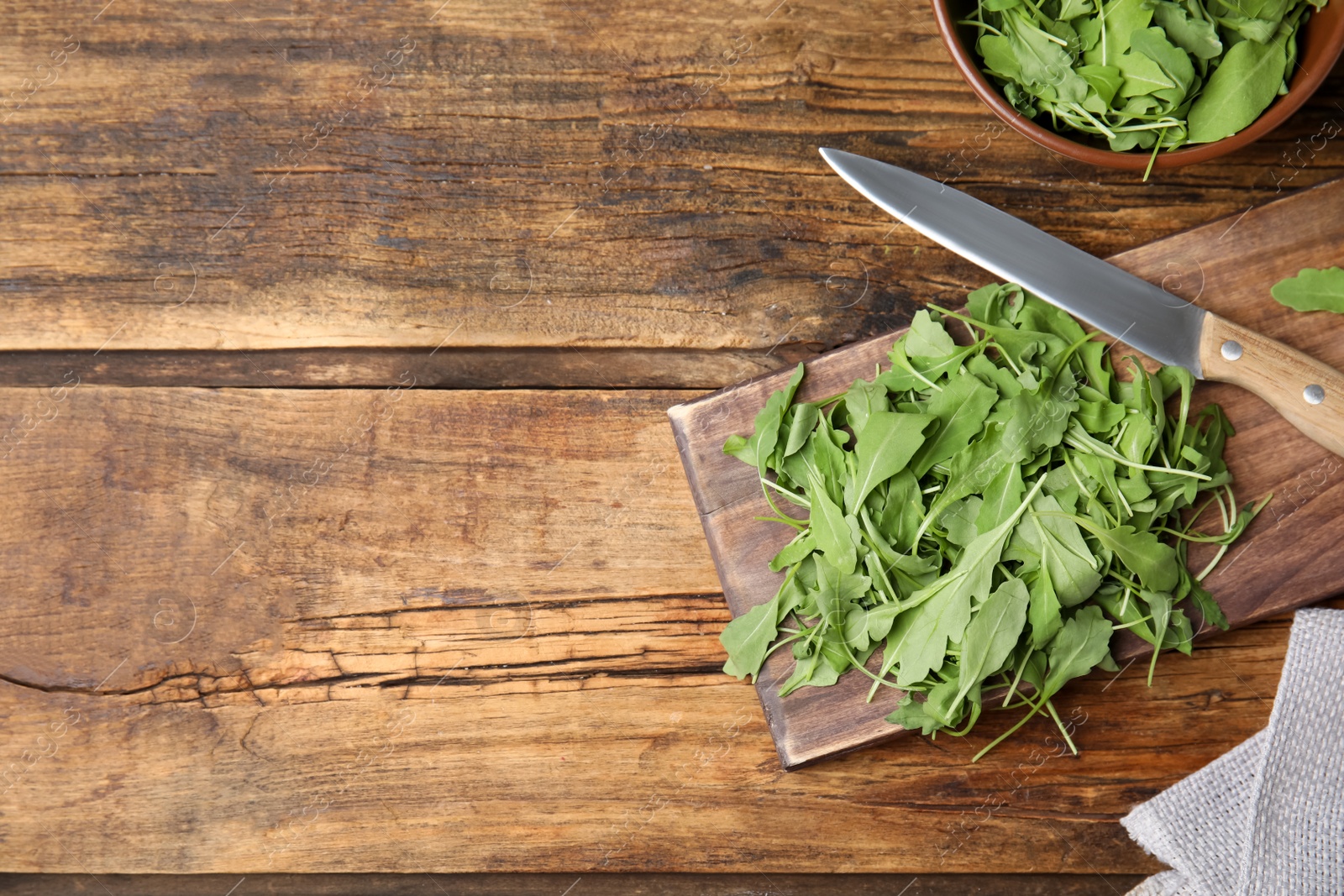 Photo of Cutting board with fresh arugula leaves and knife on wooden table, flat lay. Space for text