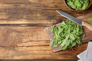 Photo of Cutting board with fresh arugula leaves and knife on wooden table, flat lay. Space for text