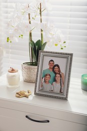 Photo of Framed family photo and orchid flower on white drawer indoors