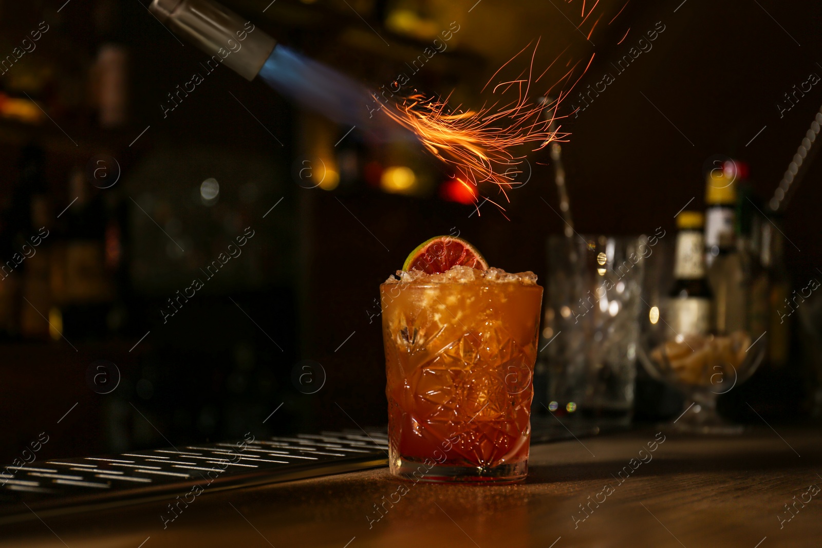 Photo of Preparing fresh alcoholic cocktail with flame at bar counter