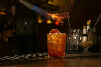 Photo of Preparing fresh alcoholic cocktail with flame at bar counter