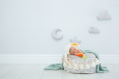 Photo of Adorable newborn child wearing bunny ears hat in baby nest indoors. Space for text