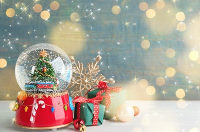 Image of Beautiful snow globe, gift boxes and Christmas decor on white table, space for text. Bokeh effect