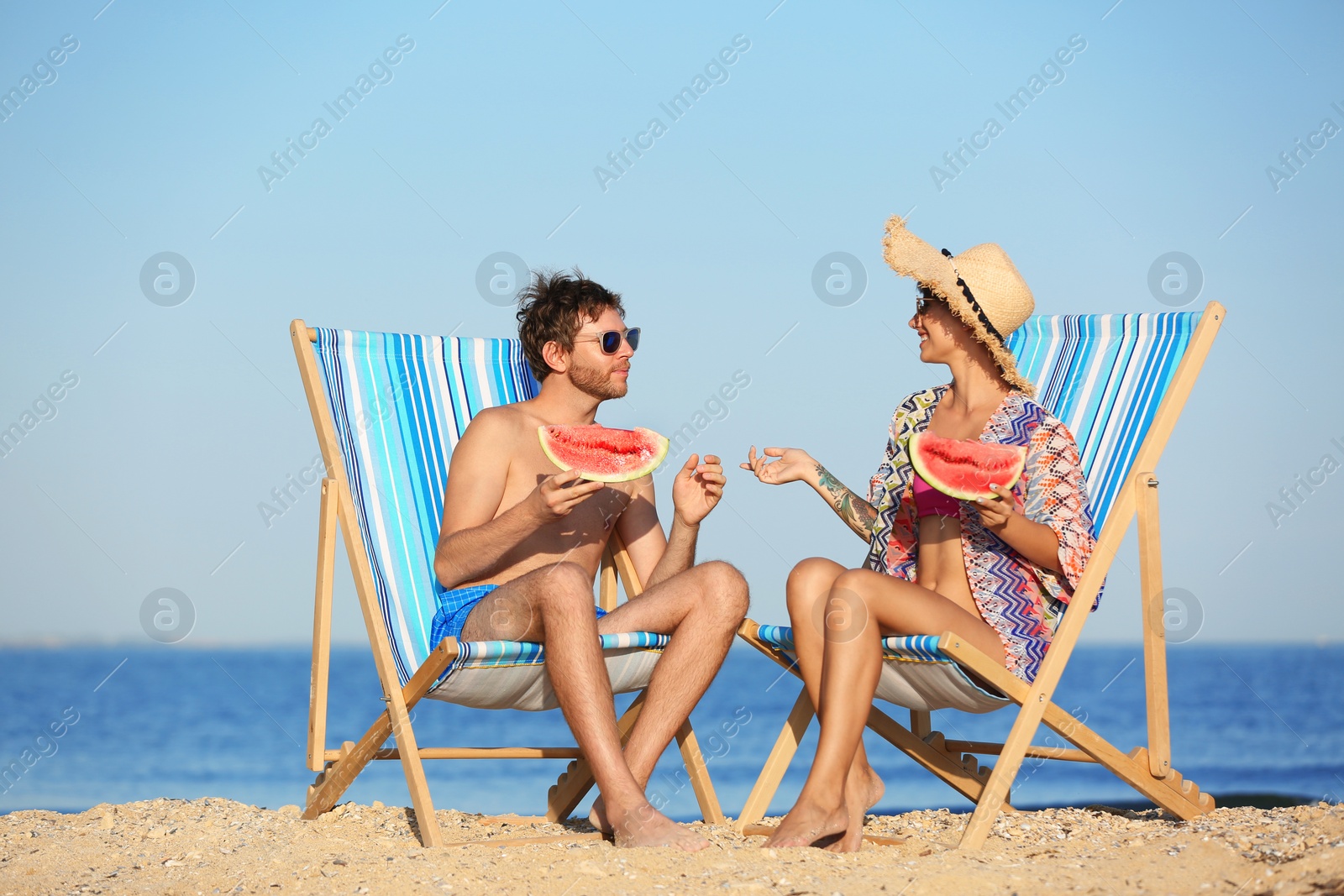 Photo of Young couple with watermelon slices in beach chairs at seacoast