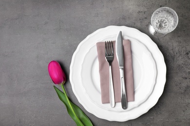 Elegant table setting with tulip on grey stone surface, top view