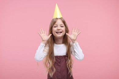 Happy little girl in party hat on pink background