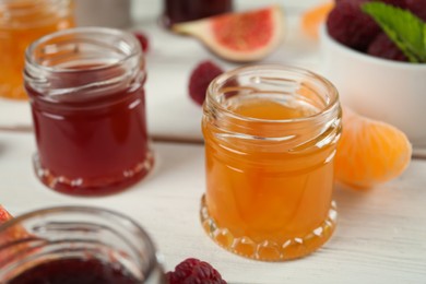 Jars with different sweet jams on white wooden table, closeup