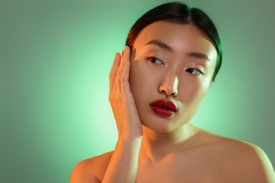 Portrait of beautiful young Asian woman on green background, space for text