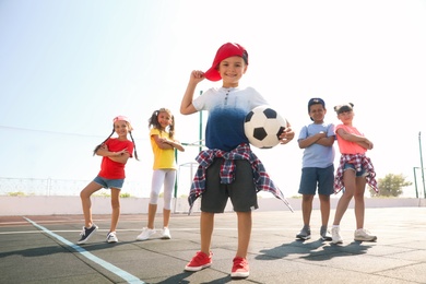 Photo of Cute children with soccer ball at sports court on sunny day. Summer camp