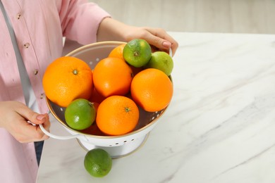 Photo of Woman holding colander with fresh fruits at white marble table, closeup. Space for text