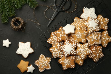 Photo of Tasty Christmas cookies with icing, scissors and spool of thread on black table, flat lay