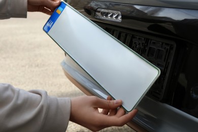 Photo of Woman installing vehicle registration plate outdoors, closeup