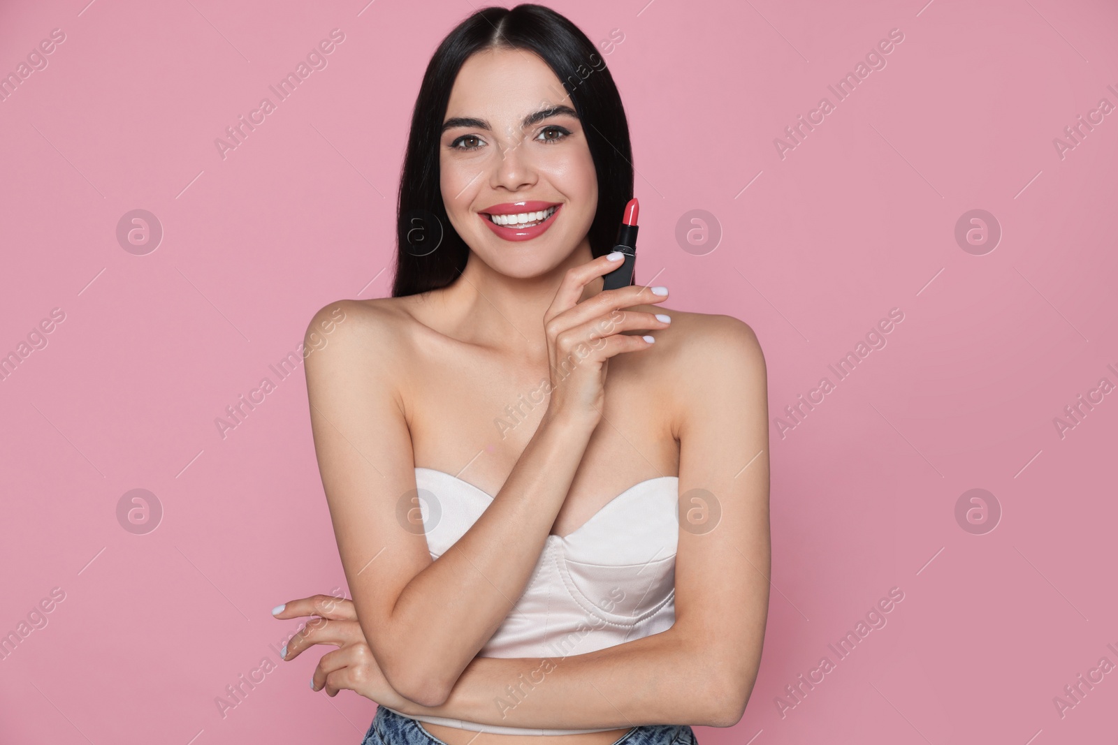 Photo of Young woman with beautiful makeup holding glossy lipstick on pink background