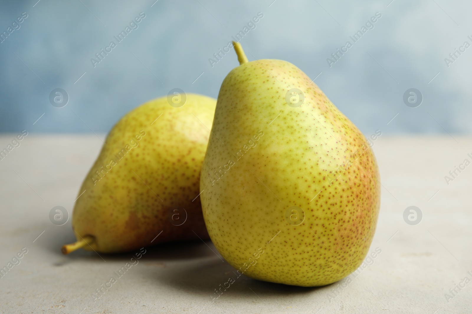 Photo of Ripe juicy pears on grey stone table against blue background, closeup