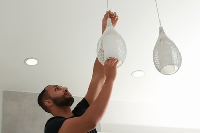 Young man repairing ceiling lamp indoors, low angle view. Space for text
