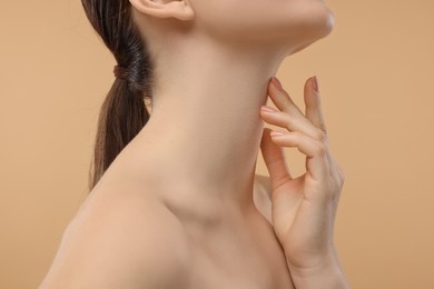 Woman touching her neck on beige background, closeup