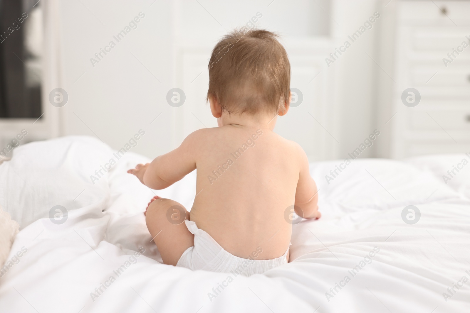 Photo of Baby boy sitting on bed at home, back view