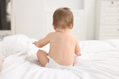 Photo of Baby boy sitting on bed at home, back view