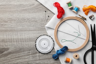 Photo of Embroidery hoop, fabric and other accessories on wooden table, flat lay. Space for text