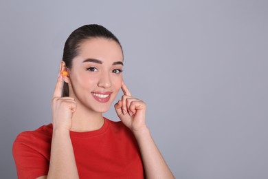 Photo of Young woman inserting foam ear plugs on grey background. Space for text