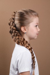 Photo of Little girl with braided hair on light brown background