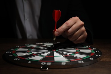 Photo of Business targeting concept. Man with dart aiming at dartboard at table in darkness, closeup