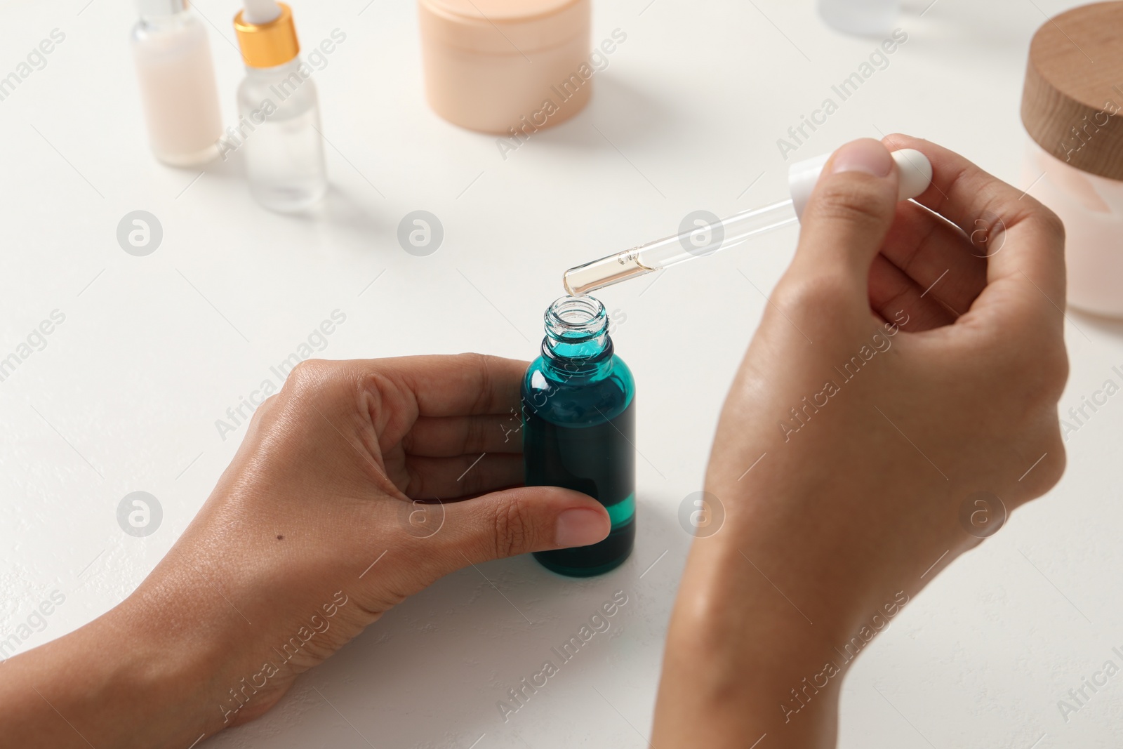 Photo of Woman with bottle of cosmetic serum at white table, closeup